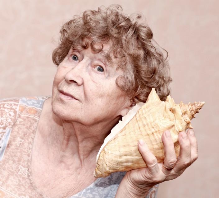 Smiling great grandmother listening to a seashell